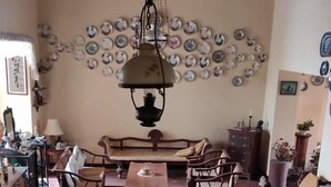 A dining area with a round wooden table, chairs, a chandelier, a sofa, and a wall decorated with plates. - Beatrice House (Galle)