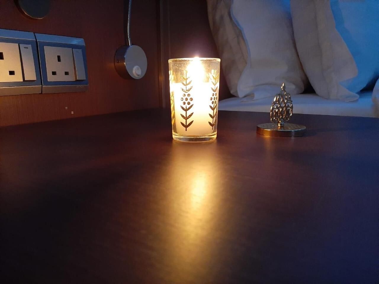 A candle on a table with a power outlet and a wall socket in the background.