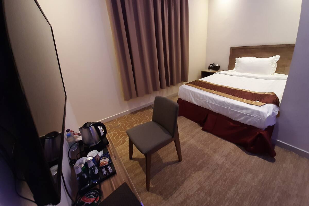 Een hotelkamer met een bed, een stoel, een bureau met koffiezetapparaat en een nachtkastje.