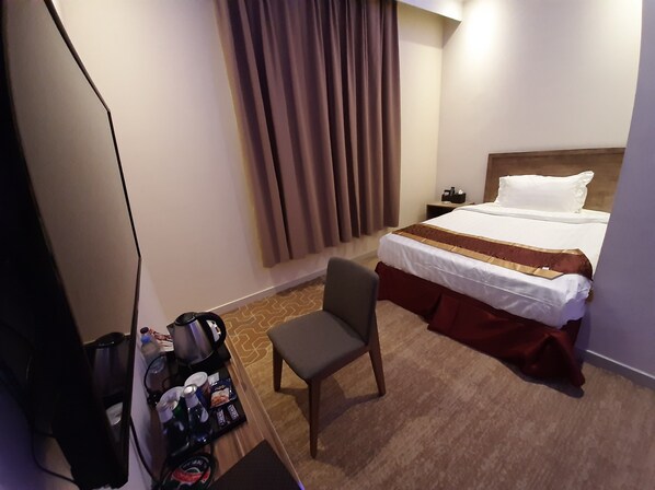 A hotel room with a bed, a chair, a desk with a coffee maker, and a nightstand.