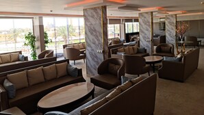 Een moderne hotel lobby met zitgedeeltes, marmeren zuilen en grote ramen met uitzicht op palmbomen en gebouwen.