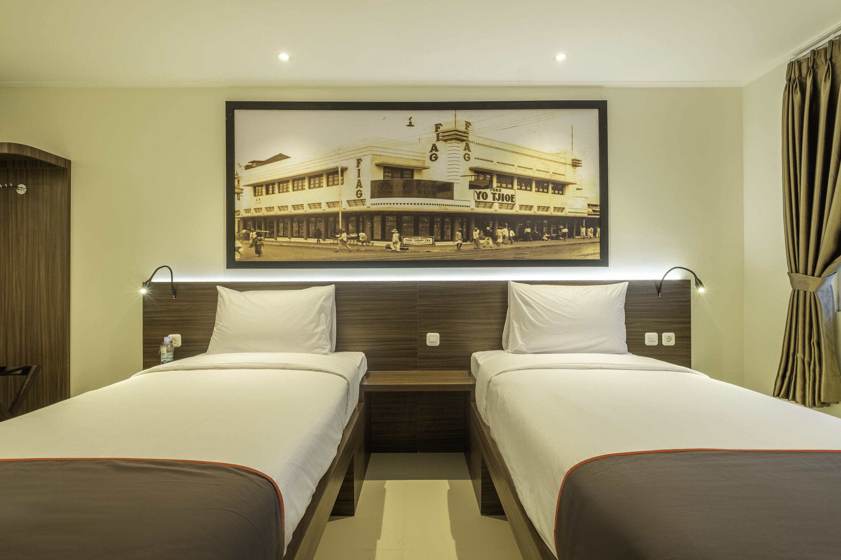 A hotel room with two beds, a large framed picture on the wall, and a wooden headboard.