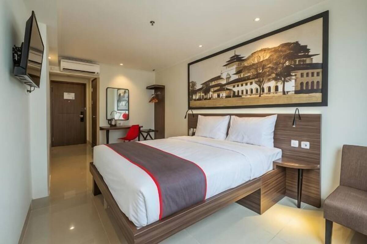 Habitación de hotel con cama, escritorio, silla, televisor y un cuadro en la pared.