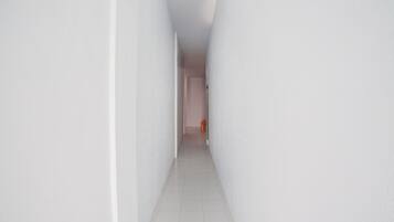 A narrow, white-walled hallway with a tiled floor leading to a door at the end.