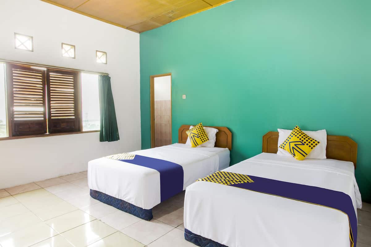 A room with two beds, a window with shutters, and a teal wall.