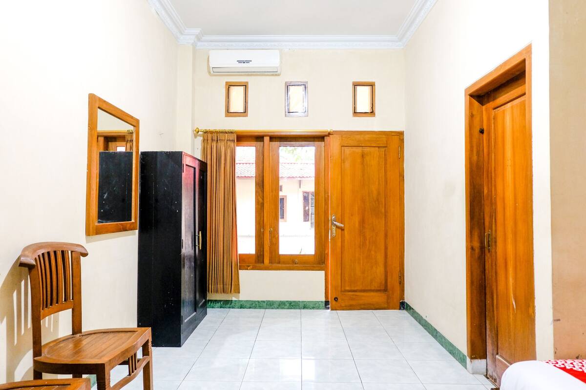 Un passadís amb una porta de fusta, un mirall, una cadira i una finestra amb cortines.