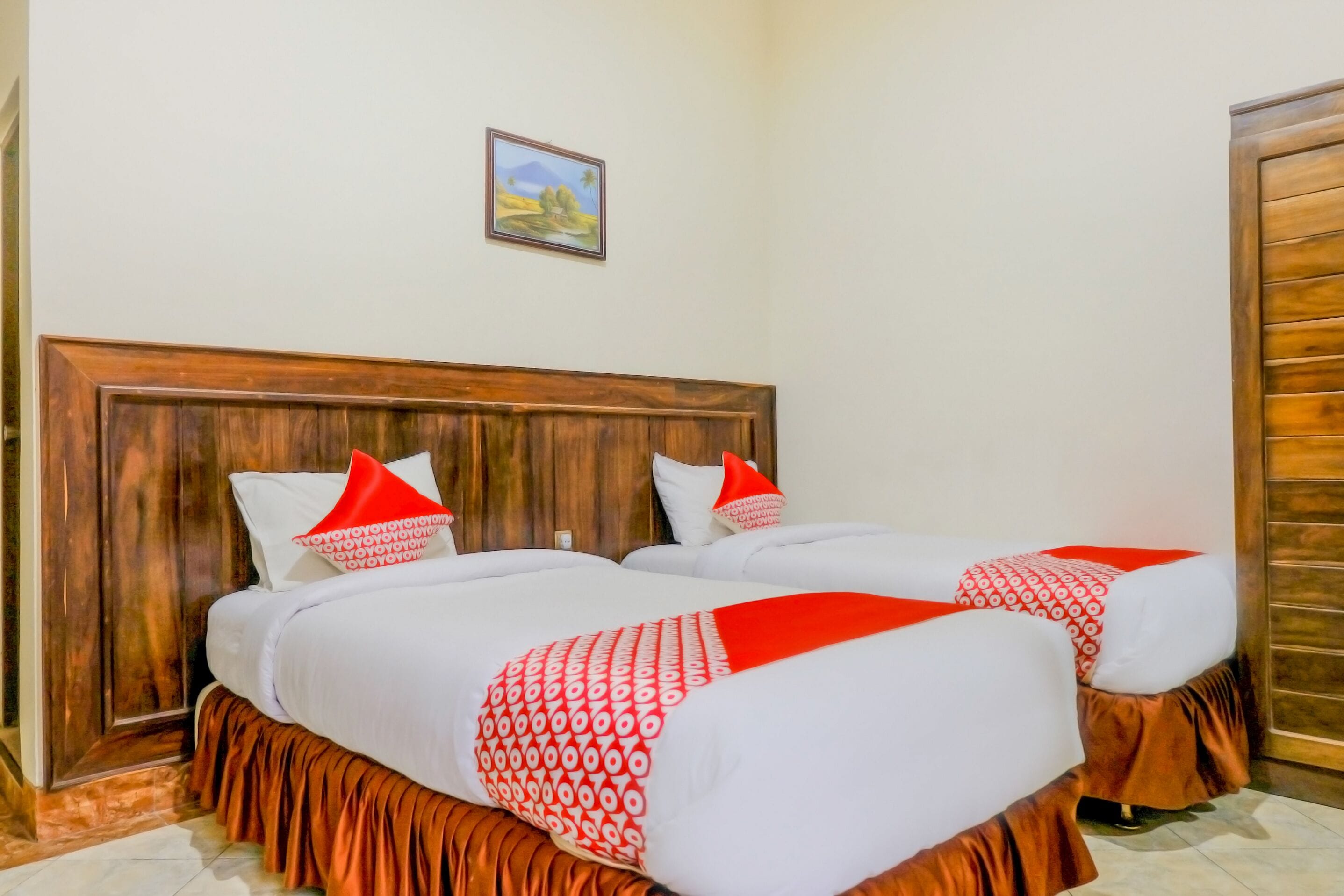A double bed with a wooden headboard, white bedding, and red accents.