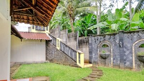 A courtyard with a stone staircase leading to a covered area, surrounded by lush greenery and a stone wall with decorative arches.