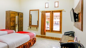 A hotel room with a bed, a desk, a chair, a mirror, and a window with curtains.