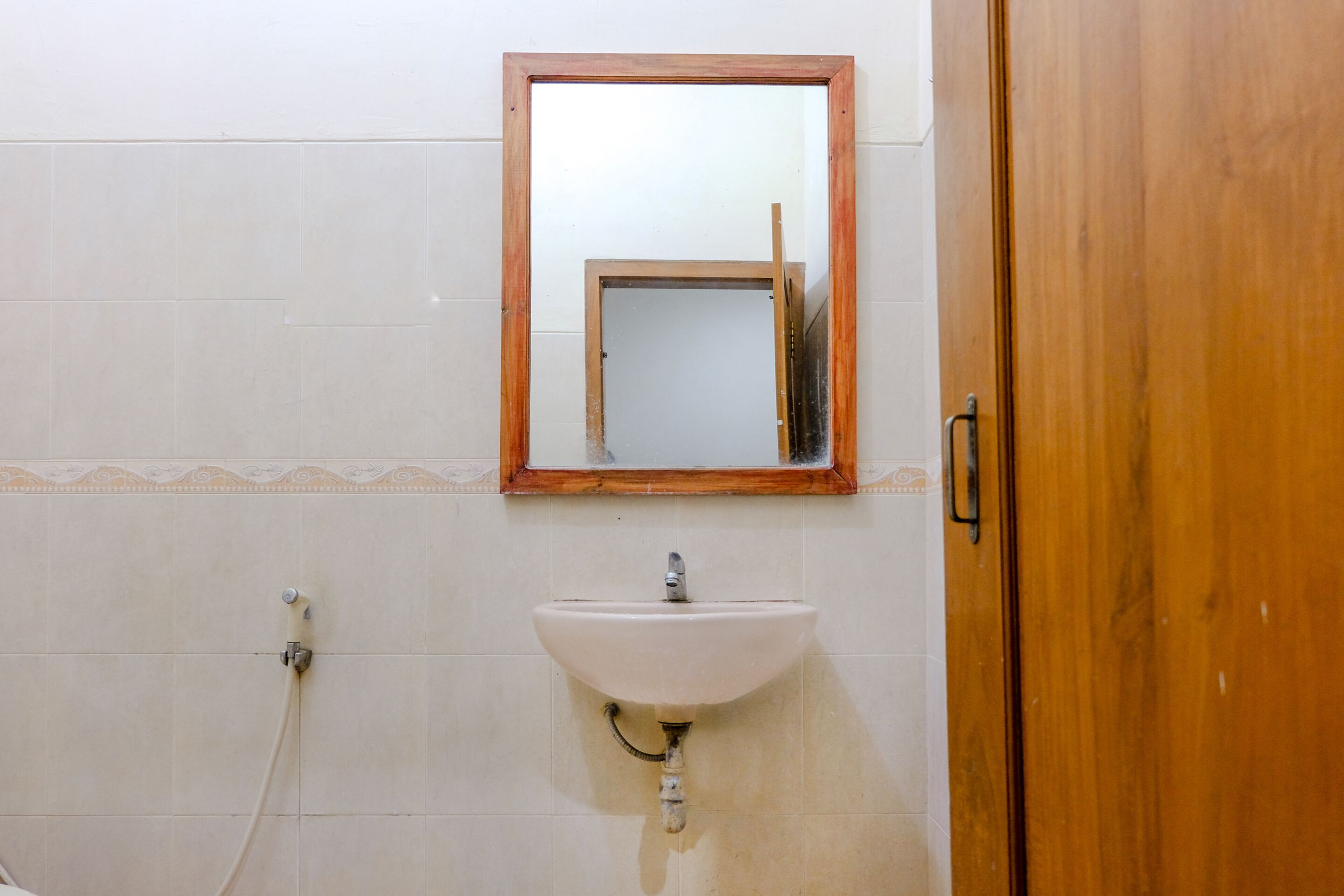 A bathroom with a white sink, a wooden door, and a mirror with a wooden frame.