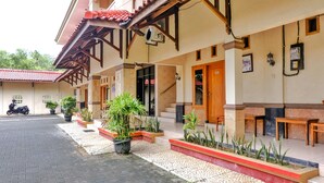 A hotel entrance with a tiled roof, potted plants, and a paved driveway.