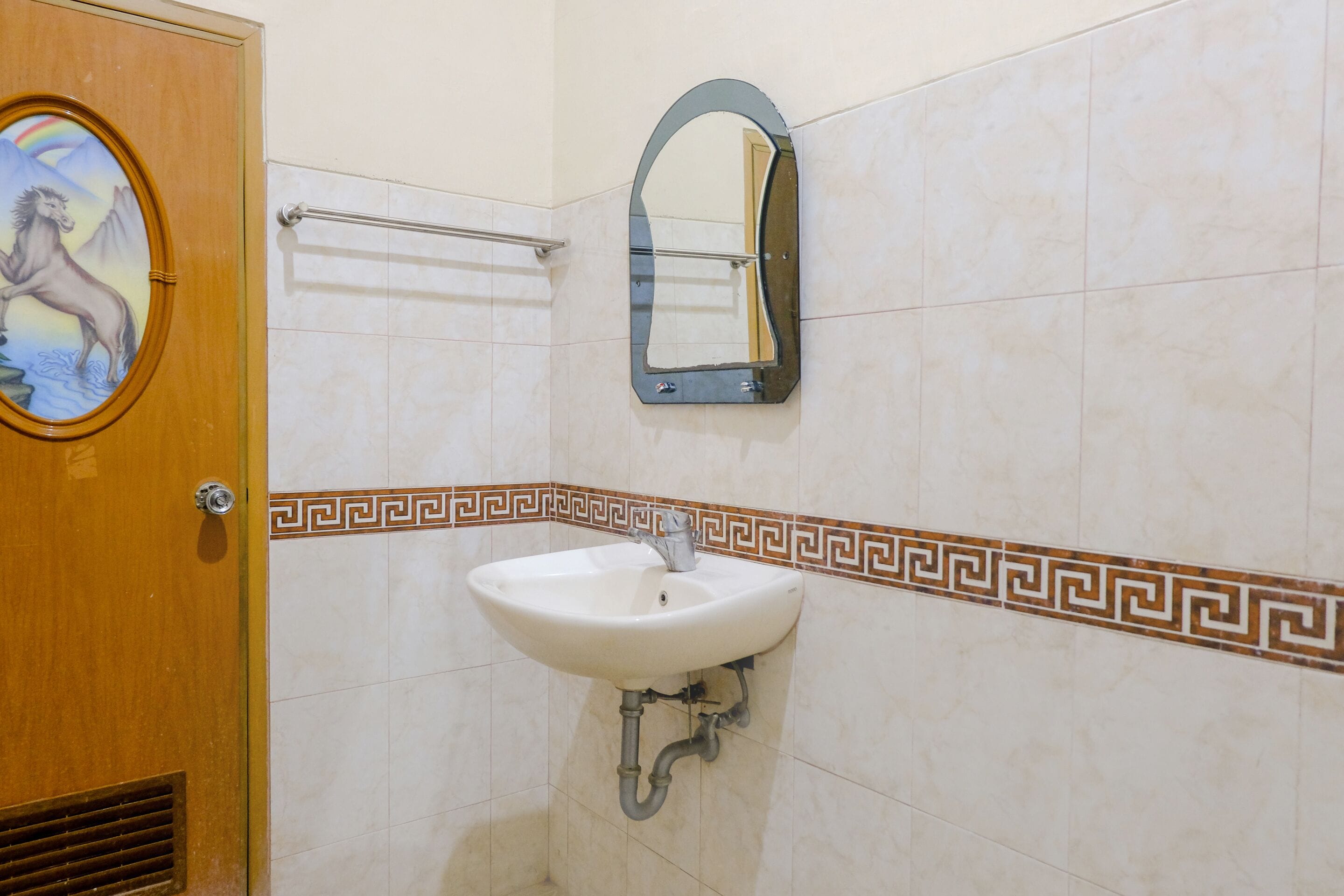A bathroom with a wooden door, a white sink with a mirror above it, and decorative tiles.