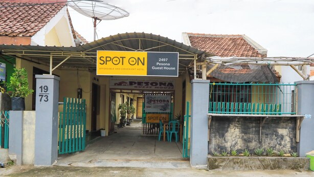 Een hotelentree met een bord waarop staat 'SPOT ON Betaalbaar en Gunstig Hotel' en 'Pesona Guest House'.