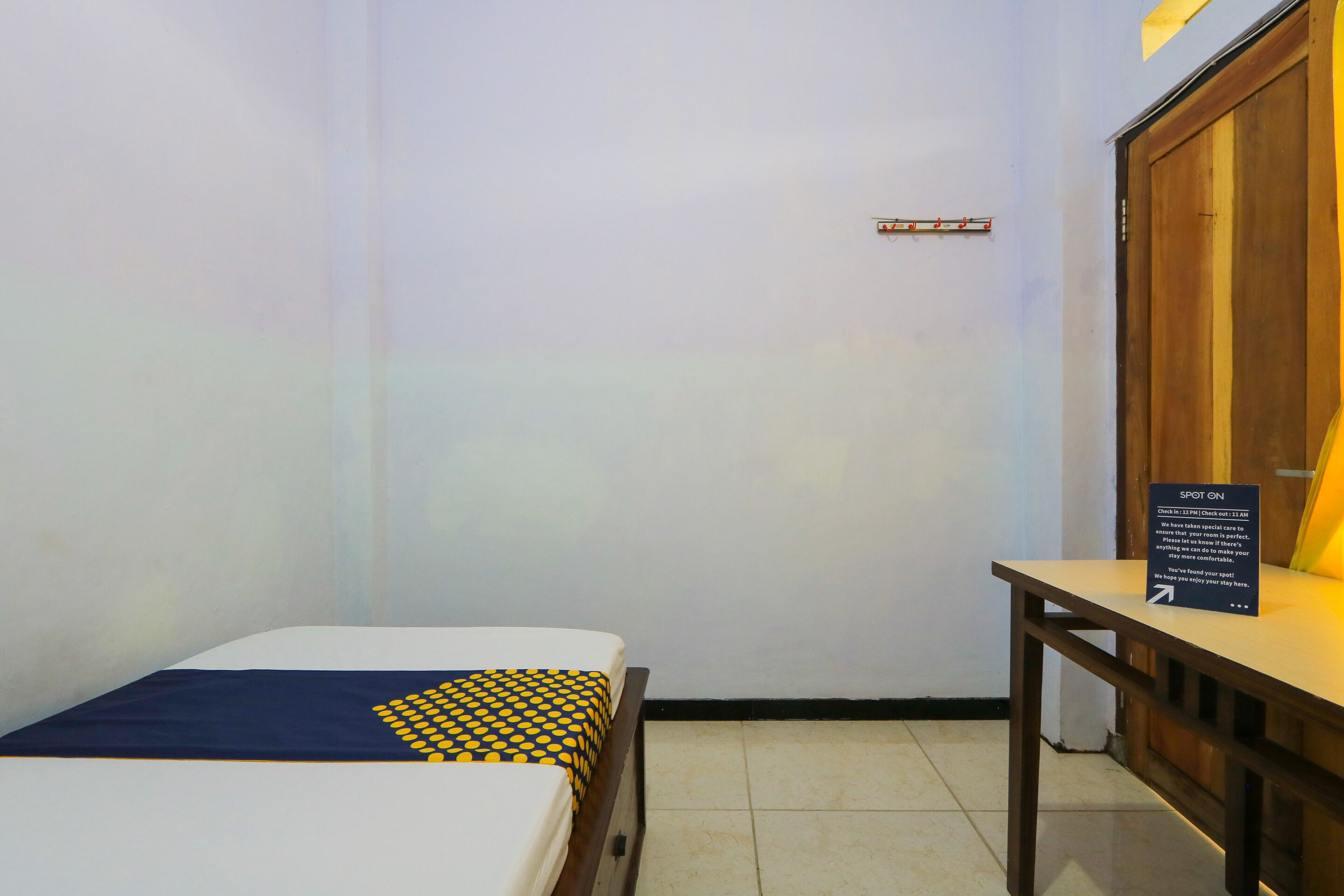 Um quarto pequeno com uma cama, uma mesa de madeira e um aviso na parede.