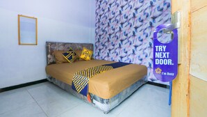 Een slaapkamer met een bed, behang met een patroon en een deur met een bordje.