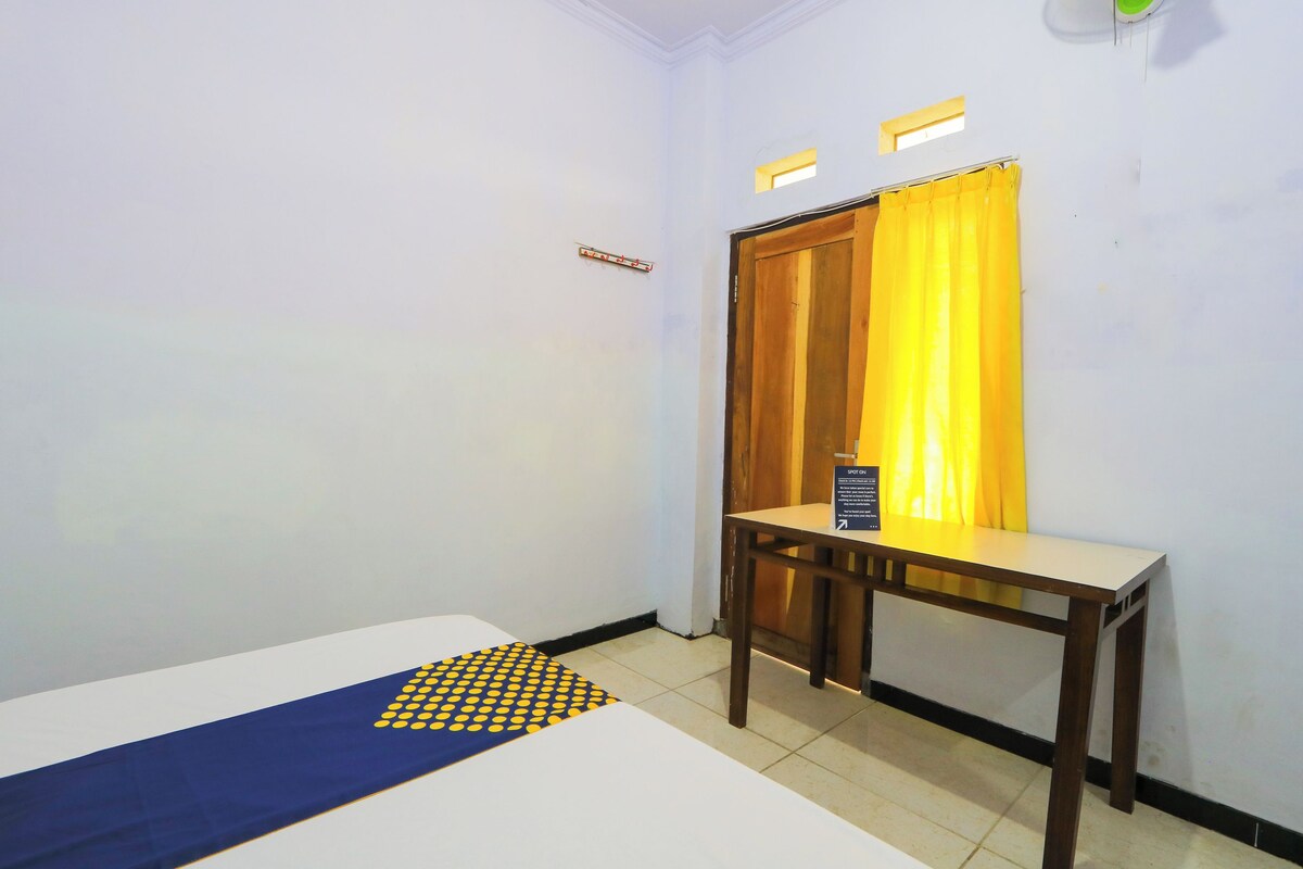 A small, clean room with a bed, a wooden table, and a yellow curtain.