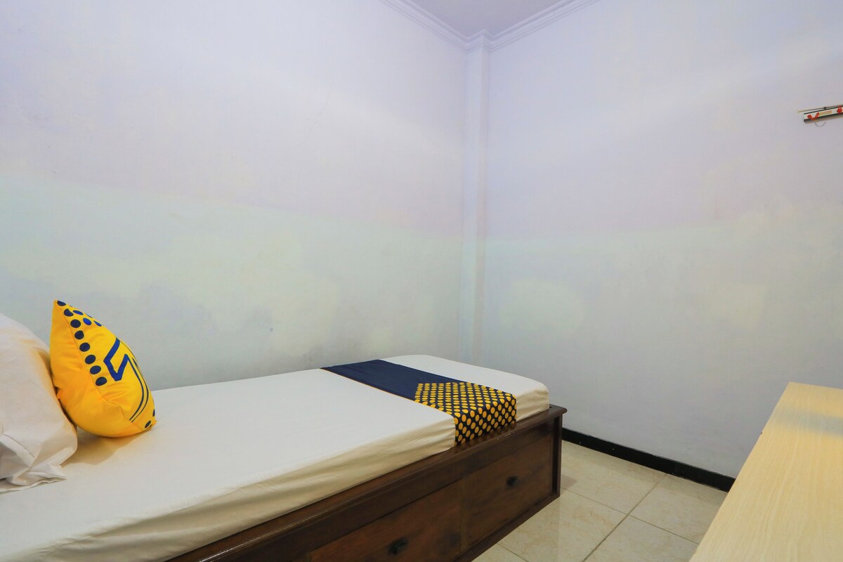 Una cama individual con estructura de madera, ropa de cama blanca y dos almohadas decorativas.