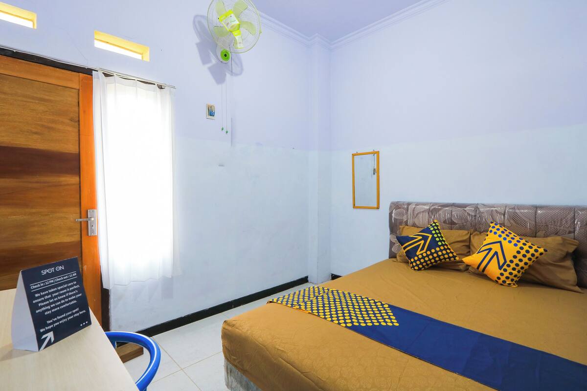 A hotel room with a bed, a wooden door, a white curtain, a ceiling fan, and a sign indicating the room is occupied.