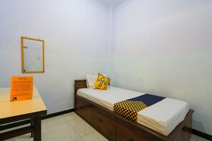 A single bed with a wooden frame, white bedding, and a yellow and black patterned blanket. A small table with a sign is in front of the bed. - OYO 2497 Pesona Guest House (Banyuwangi)