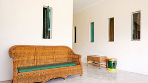 A wicker sofa with a green cushion in a room with tiled flooring and a white wall. - OYO 2614 Demasto Homestay (Jember)