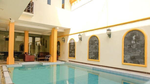 An indoor swimming pool with clear water, yellow and white walls, and arched windows. - OYO 2614 Demasto Homestay (Jember)