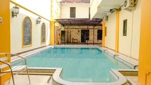 A swimming pool with a tiled deck, a covered seating area, and a yellow and white building facade. - OYO 2614 Demasto Homestay (Jember)