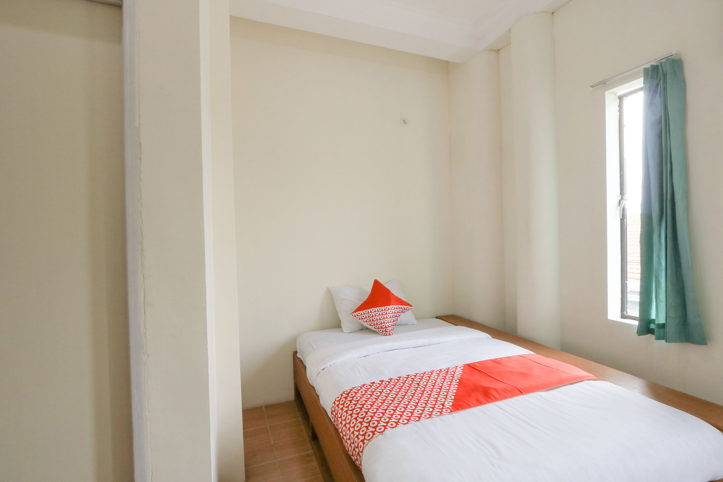 A small, neatly arranged bedroom with a single bed, a window with curtains, and a plain wall.