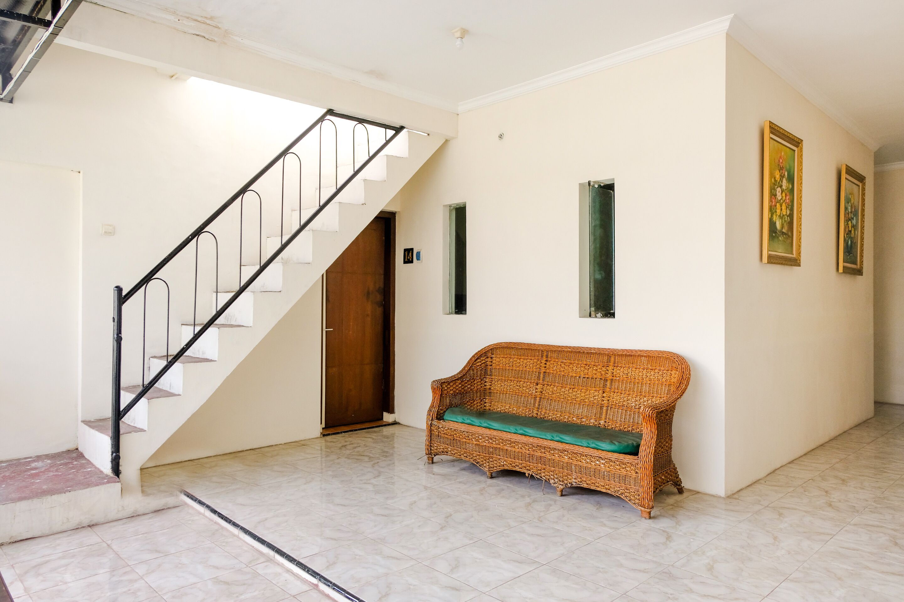 A staircase with a metal railing, a wicker sofa with a green cushion, and two framed pictures on the wall.