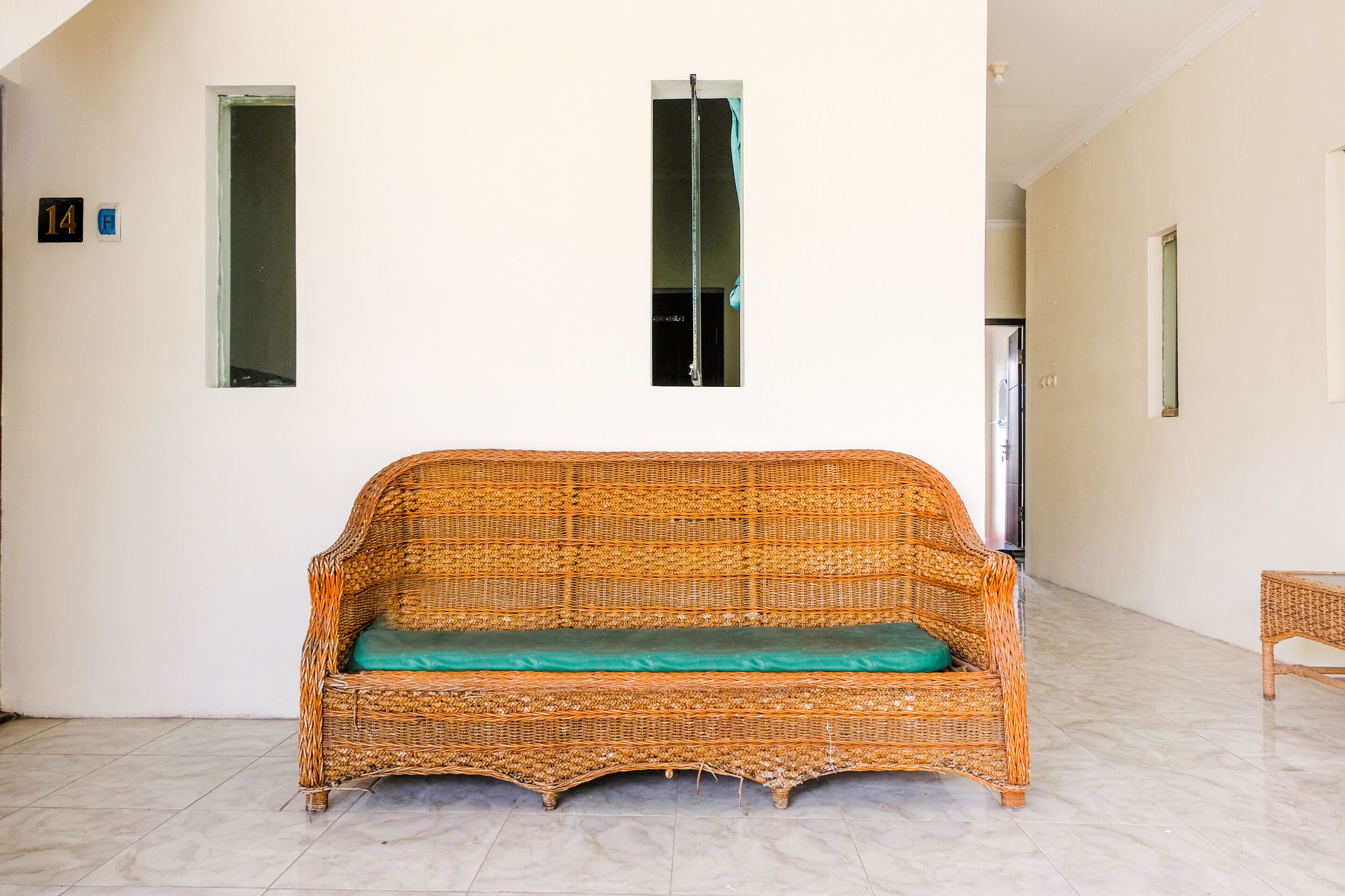 A wicker sofa with a teal cushion in a hallway with white walls, a door, and a small table.