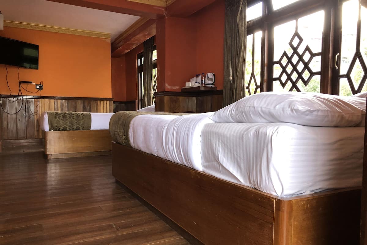Ein Hotelzimmer mit einem hölzernen Bett, einer kleinen Sitzecke, einem an der Wand befestigten Flachbildfernseher und einem Fenster mit Gittermuster.