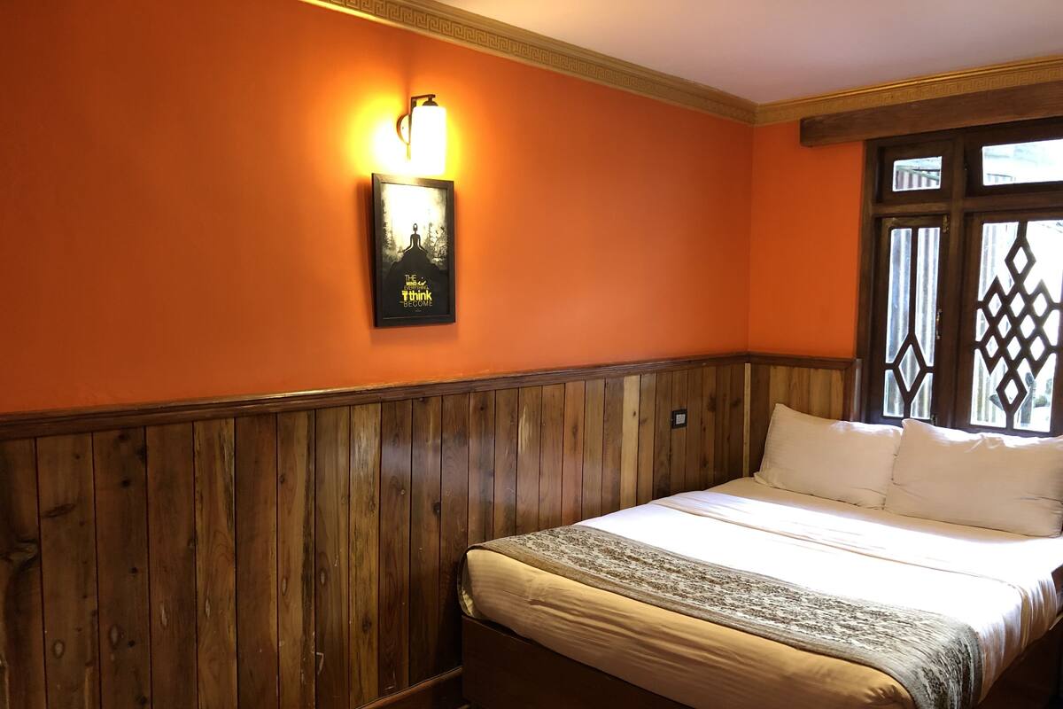Ein Schlafzimmer mit einem hölzernen Kopfteil, einem Bett mit weißer Bettwäsche, einer Wandleuchte und einem gerahmten Zitat an der Wand.