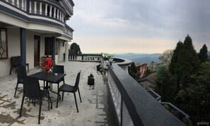A terrace with a table and chairs, a potted plant, and a view of the mountains. - The Rope Resort (Darjeeling)