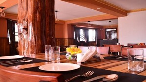 Un espace repas avec des tables en bois, des sets de table noirs et des verres transparents.