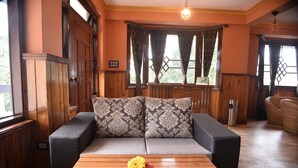 Une pièce chaleureuse avec un canapé en bois, une table basse en bois ornée d’un vase de fleurs et des chaises en osier.