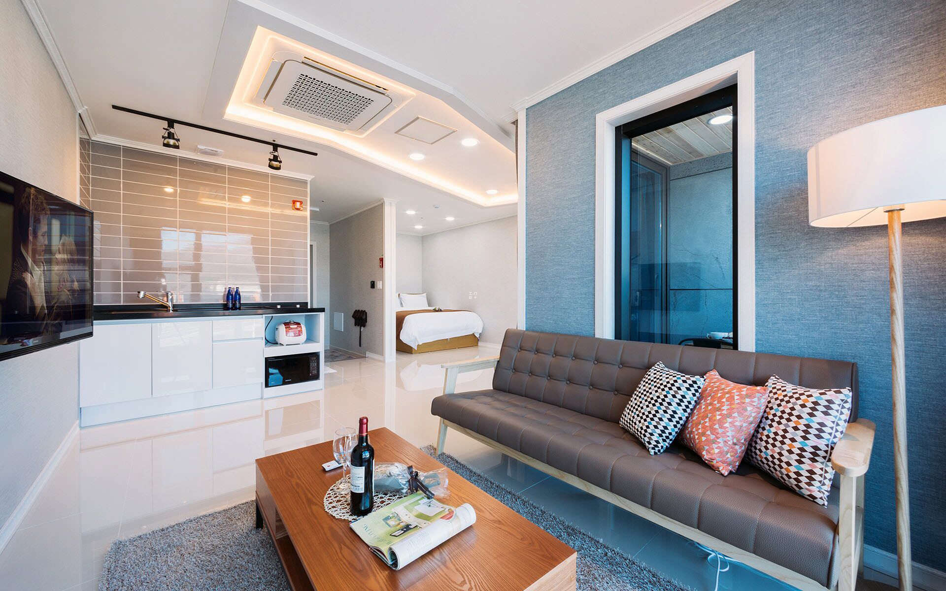 Una sala de estar moderna con sofá, mesa de centro y una zona de cocina con mostrador y armarios.