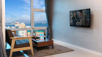 A modern living room with a large window, a sofa, a coffee table, and a TV mounted on the wall.