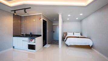 A modern hotel room with a bathroom, a bed, and a kitchenette.