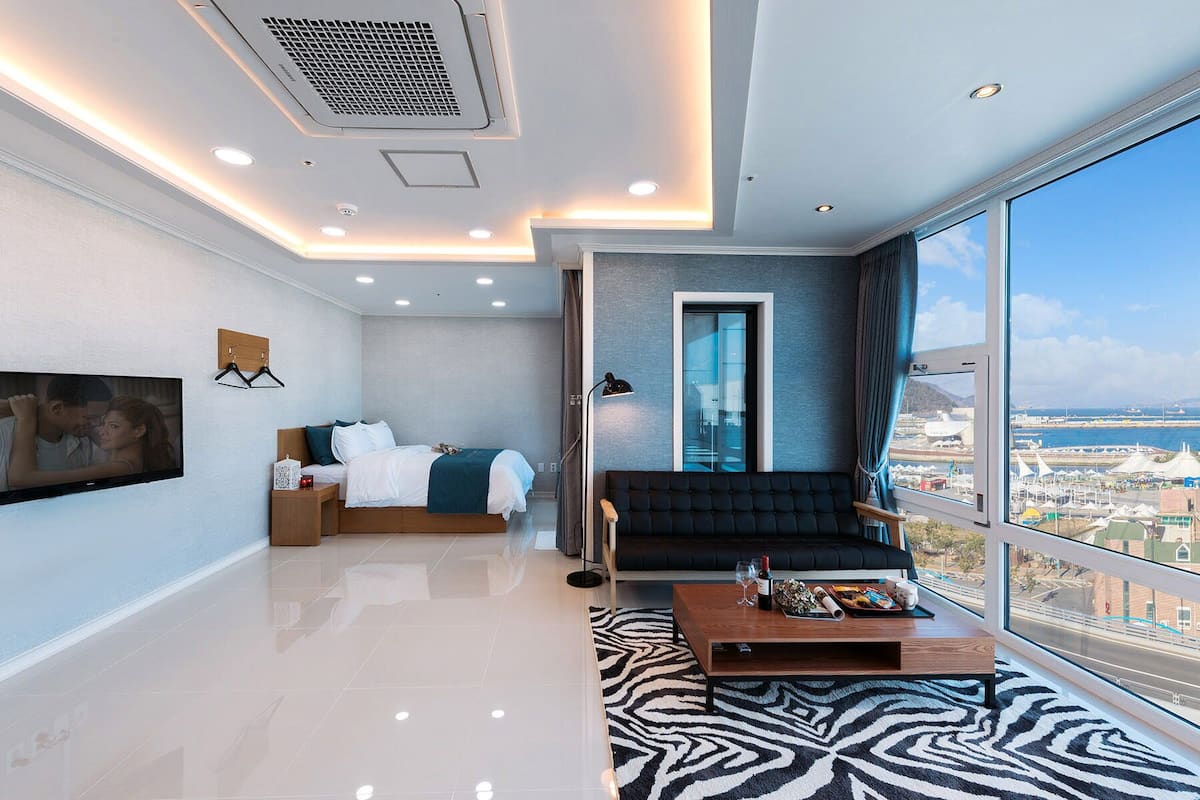 Quarto de hotel moderno com uma cama grande, um sofá, uma mesa de centro e uma televisão.