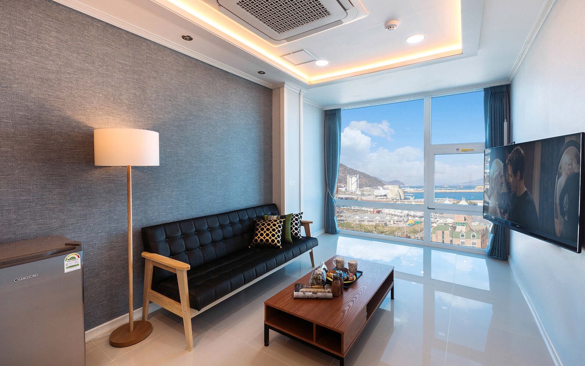 A modern living room with a black sofa, a wooden coffee table, and a TV on a wall.