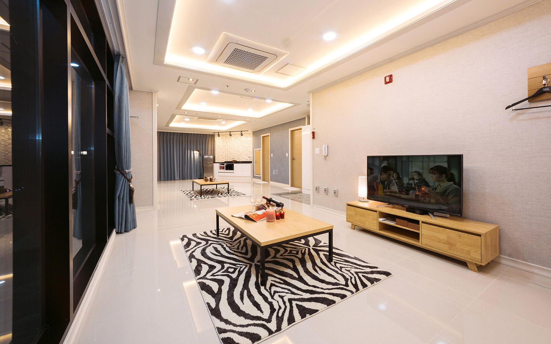 A modern living room with a flat-screen TV, wooden entertainment unit, and a zebra-patterned rug.