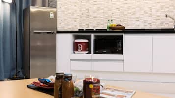 A kitchen with a stainless steel refrigerator, a rice cooker, and a microwave. There are jars on the counter and a candle.