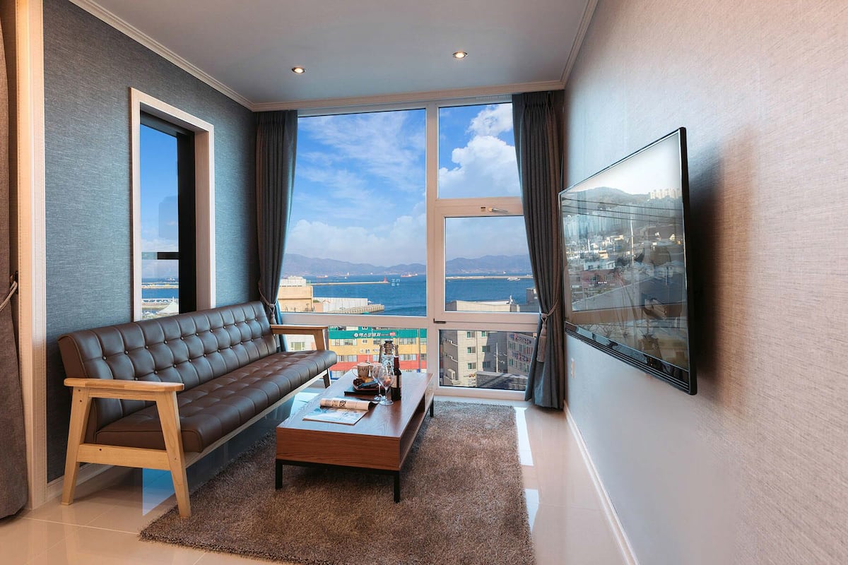 Uma sala de estar moderna com um sofá de couro, uma mesa de centro de madeira e uma televisão grande na parede.