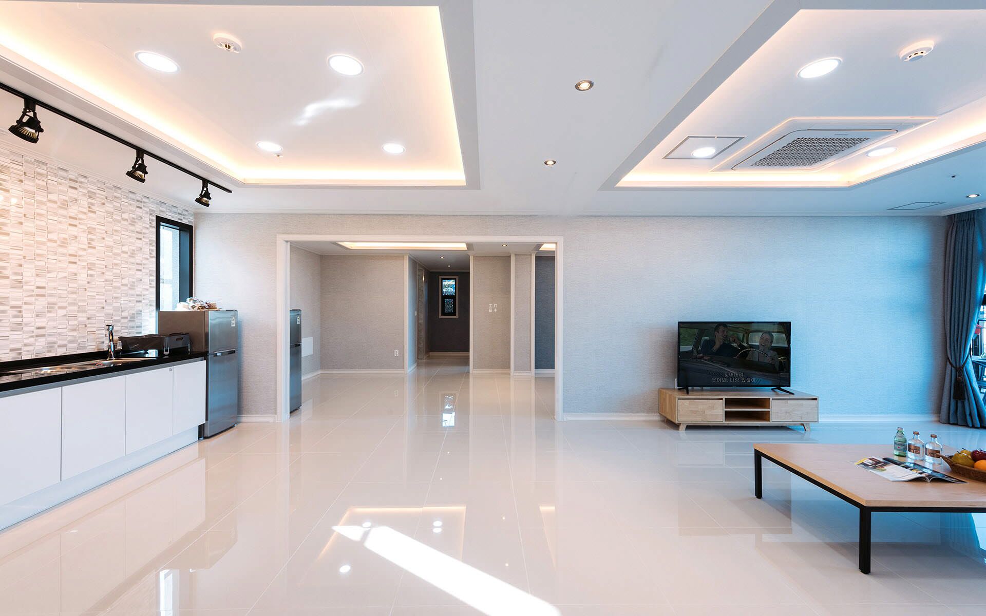 A modern living room with a kitchen area, a flat-screen TV, and a dining table.