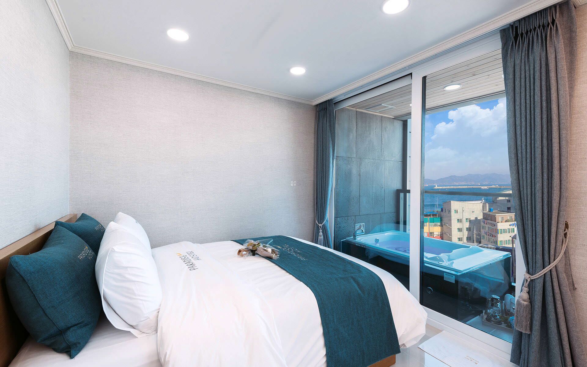 Una habitación de hotel moderna con una cama, vistas de la ciudad a través de un ventanal grande y un balcón con barandilla de vidrio.
