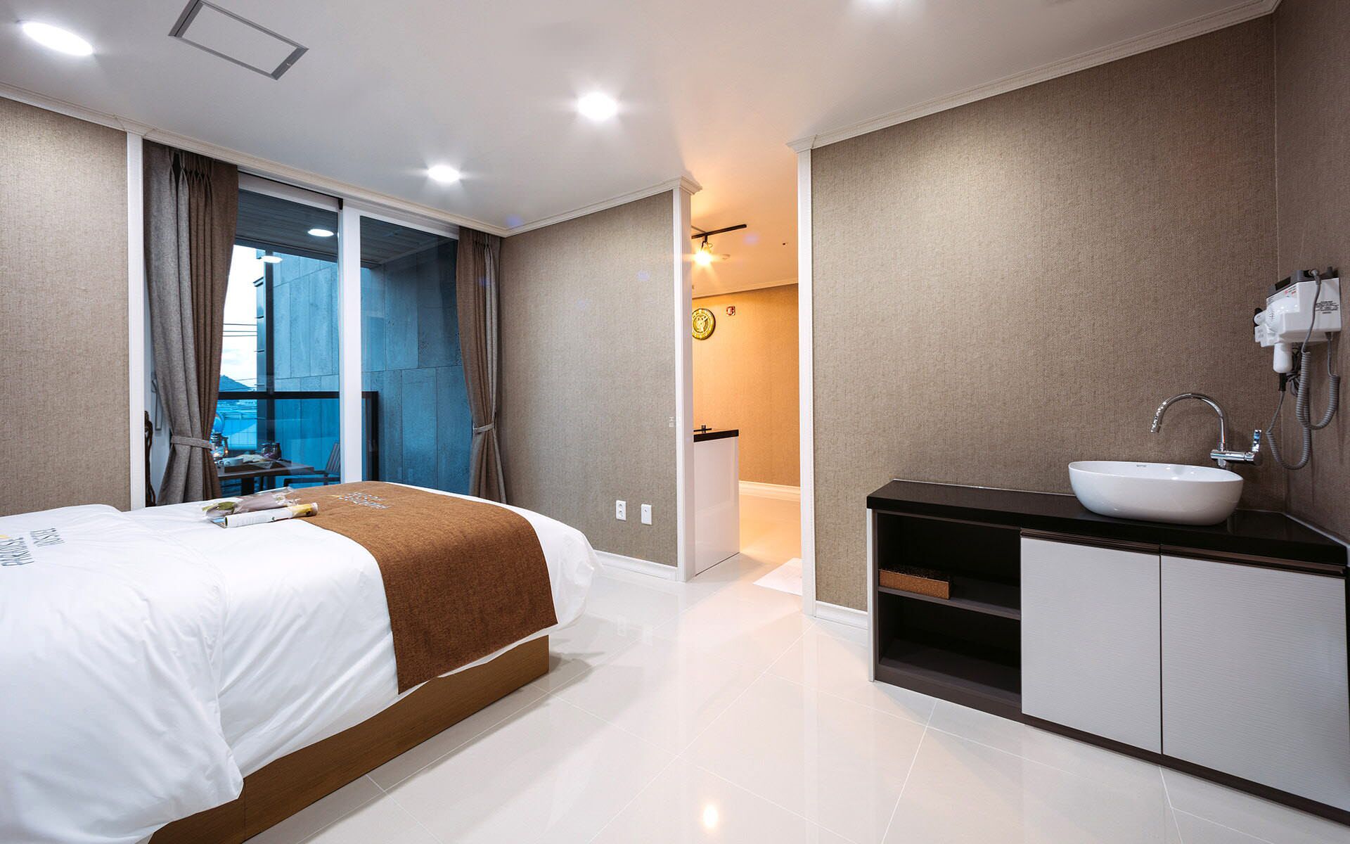 A modern hotel room with a large bed, a bathroom with a sink and mirror, and a view of the city through the window.