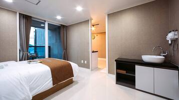 A modern hotel room with a large bed, a bathroom with a sink and mirror, and a view of the city through the window.