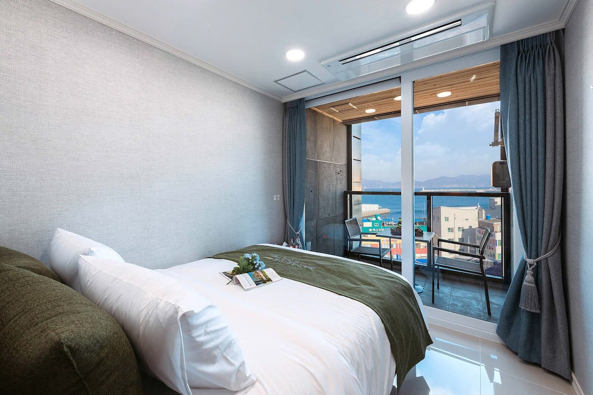 Quarto de hotel moderno com uma cama grande, uma varanda com vista para a cidade e uma janela com cortina.