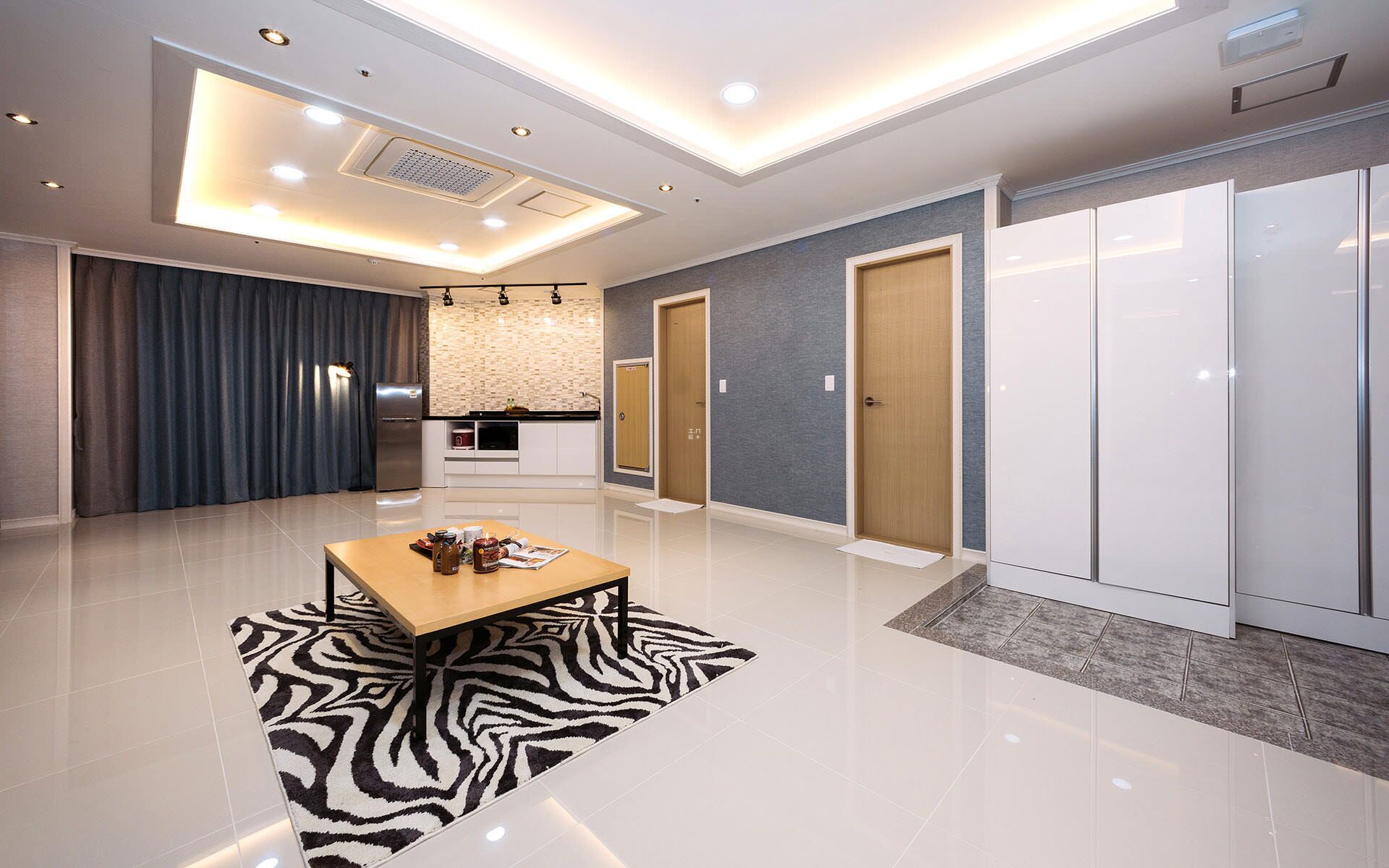 A modern hotel room with a kitchen area, a dining table with a zebra-patterned rug, and a wardrobe.