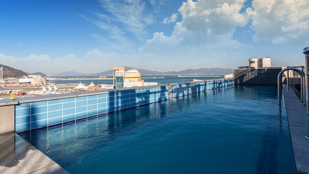 A swimming pool with a view of a coastal cityscape, including a bridge and distant mountains.