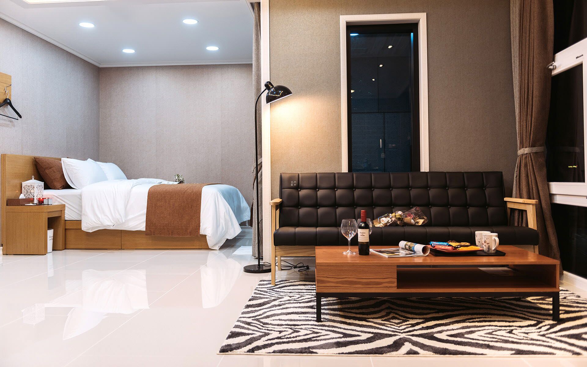 Une chambre à coucher moderne avec un lit, une table de chevet et un canapé noir accompagné d’une table basse.